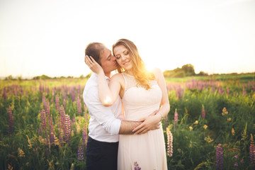 Fototapeta premium Bride holds groom's neck while he kisses her in the rays of sunset