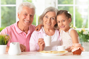 Obraz na płótnie Canvas grandparents with granddaughter drinking tea 