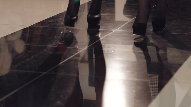 Legs of two women catwalking synchronously on the heels. Slowly