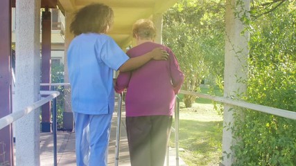 Old woman with crutches helped by nurse outdoor