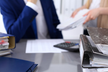 Binders with papers are waiting to be processed with businessman and secretary back in blur. Accounting planning budget, audit, insurance  and business concept