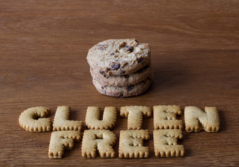 The phrase Gluten Free spelled out with alphabet shaped cookies or biscuits with a stack of cookies in the background and on a wooden table top.