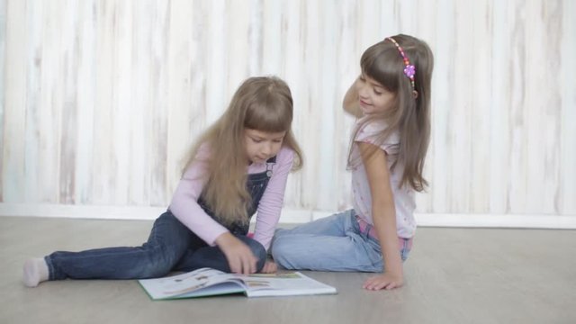 two little girls reading a book lying on the floor