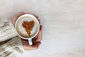love warms/ frothy cappuccino with heart pattern in hand and dressed up warm sweater top view