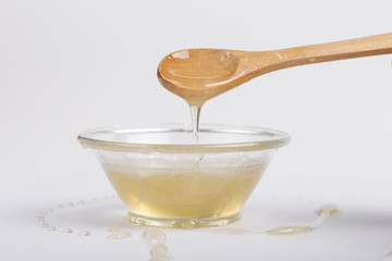 Bee honey in a glass bowl and wooden spoon on  white background