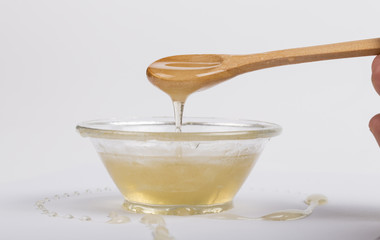 Bee honey in a glass bowl and wooden spoon on  white background