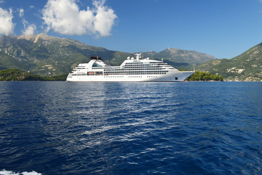 Big white cruise ship in calm blue sea, high mountains on the background, blue sky with fluffy white clouds