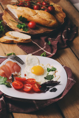 fried eggs with tomato, basil and prosciutto, table set for cozy breakfast at home