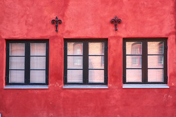 Three black painted colonial style windows of wood, fastened in a red plastered facade, with two iron wall anchors, of a townhouse in Elsinore, Denmark