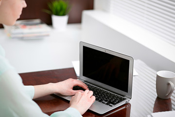 Business woman hands in a green blouse sitting at the desk in the office and typing on the laptop .
