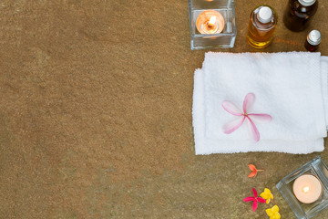 Fototapeta na wymiar Aromatic oil, burned candle, pink yellow orange flowers, white towel on vintage grunge stone background, spa treatment concept
