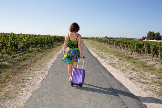 walking girl with luggage on the road in the vineyard