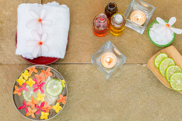 Aromatic oil, burned candle, pink yellow, orange flowers, sliced lime, white towel on vintage grunge stone background, spa treatment concept