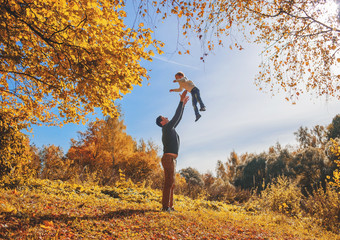 Father throw up his son in autumn forest.