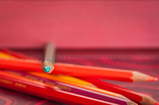 matita colore verde acquamarina sopra altri pastelli rossi e arancioni.  Sfondo rosso; immagine a fuoco sulla punta della matita Stock Photo