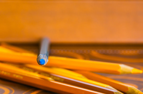 matita colore azzurro sopra altri pastelli giallo oro. Sfondo giallo; immagine a fuoco sulla punta della matita