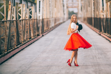 stylish portrait of a beautiful young woman on the bridge in a red skirt and black hat on a sunny day at sunset posing and smiling Life Style