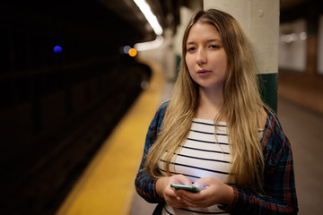 Young woman in city on subway platform texting cell phone