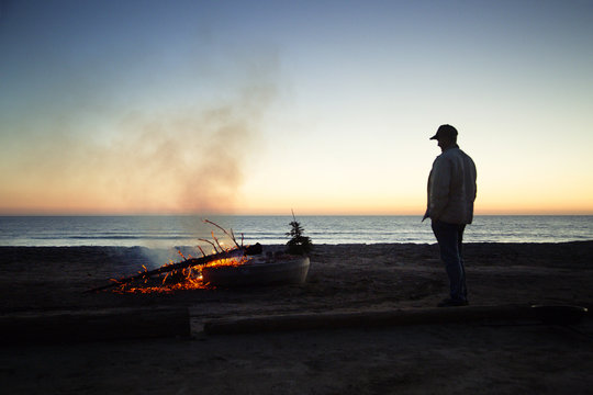 Man looking at burning wood at beach against clear sky