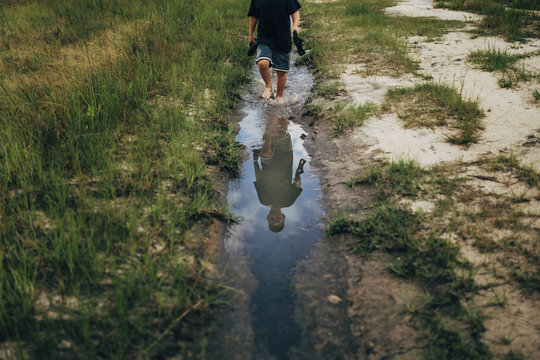Reflection of boy holding shoes while walking in puddle