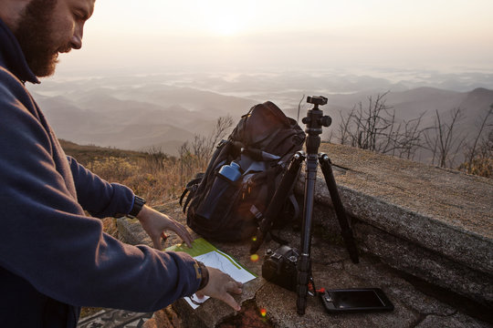 Man reading at map while standing on mountain during sunset