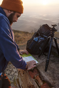 Man looking at map while standing on mountain during sunset