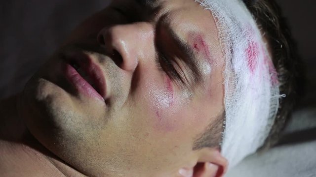man with head injuries lying on the bed. bandaged head. bruise on his face.