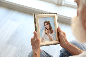 Elderly man holding photo frame with picture of young woman. Happy memories concept.