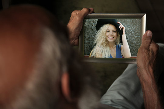 Elderly Man Holding Photo Frame With Picture Of Young Woman. Happy Memories Concept.