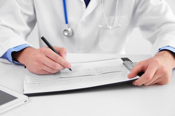 Fototapeta premium Male doctor making notes on cardiogram, close up view