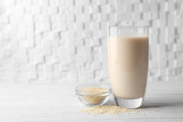 Glass of sesame milk and bowl with seeds on wooden table against white blurred background