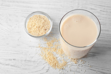 Glass of tasty sesame milk and bowl with seeds on white wooden table