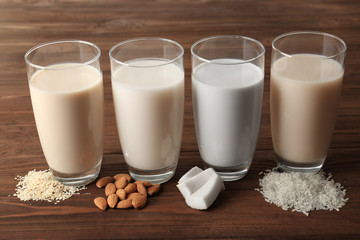 Glasses of almond, rice, sesame and coconut milk on wooden table