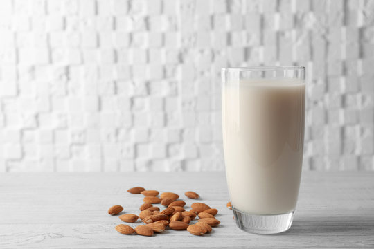 Glass of almond milk on wooden table against white blurred background