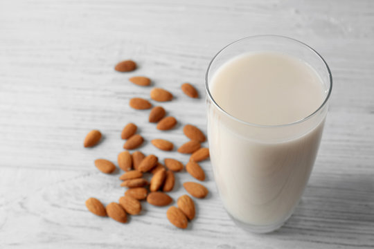 Glass of tasty almond milk on white wooden table, close up view