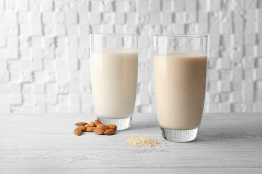 Glasses of almond and sesame milk on wooden table against white blurred background