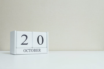 Closeup white wooden calendar with black 20 october word on blurred white wood desk and cream color wallpaper in room textured background with copy space , selective focus at the calendar