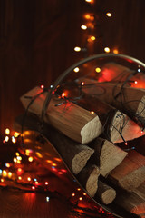 Stack of firewood and garland on blurred background, close up view