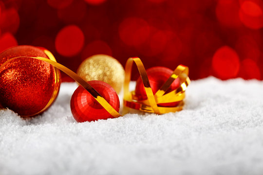 Close up view of beautiful Christmas baubles and ribbon on white snow against defocused lights