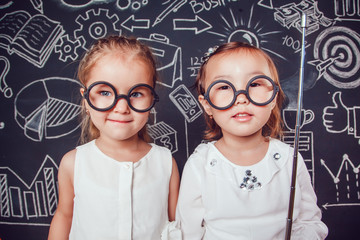 Two little smart girls in glasses holding a pointer on dark background with business or school picture