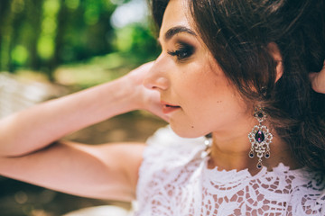 fashion outdoor photo of gorgeous bride with dark hair in luxurious wedding dress and crown posing at the park. close up. gemstone