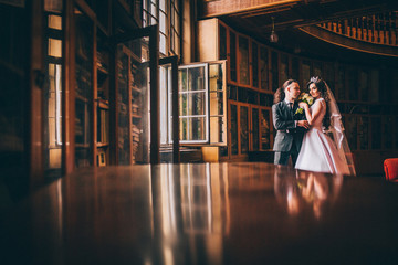 Elegant wedding couple at old library. Groom woth long hair and piercing.