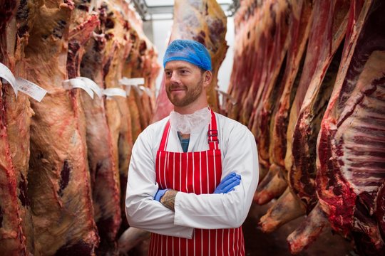 Smiling butcher standing with arms crossed in meat storage room