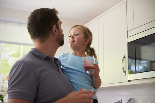 Father And Daughter Enjoying Homemade Smoothies In Kitchen