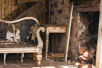 A landscape image of the inside of a derelict croft showing a Chaise Longue and the fireplace.