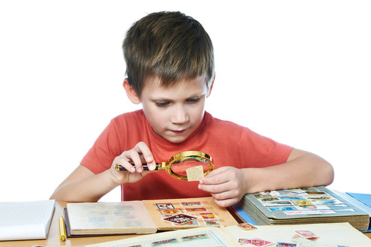 Boy with magnifier looks his stamp collection isolated