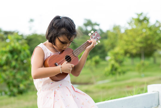 A Little Girl Playing Ukulele In The Garden.