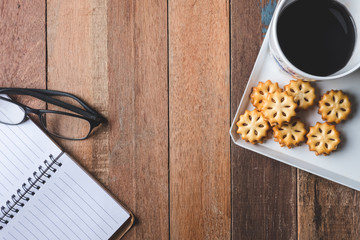 Top view of Notebook with glasses,cookie and coffee cup on wooden table.