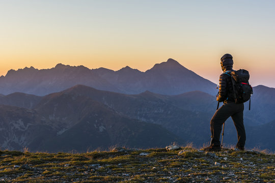 Hiker with backpack and trekking poles at sunrise.