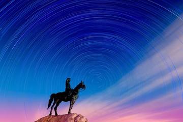 Naklejka premium Horse rider statue looking at star-trails